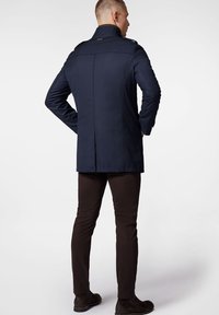 Marynarka wojskowa o wysokim kołnierzu, z pagonami na ramionach i dopasowanym kroju. Wykonana z lekkiego materiału, o długości średniej, zestawiona z brązowymi spodniami i butami.