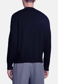 Maglione nero lavorato a maglia con scollatura a girocollo, polsini e orlo a coste, caratterizzato da una texture liscia e una vestibilità rilassata. Dettagli di design visibili sulla schiena.