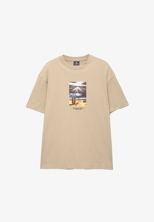 Bež majica od pamuka s kratkim rukavima, koja prikazuje središnji grafički prikaz pustinjskog krajolika s kaktusom i cestom, uz tekst ispod.