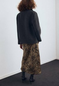 Chaqueta de lana negra con mangas amplias, combinada con una falda de satén con estampado de leopardo. Modelo con botas de tacón negras hasta la rodilla.