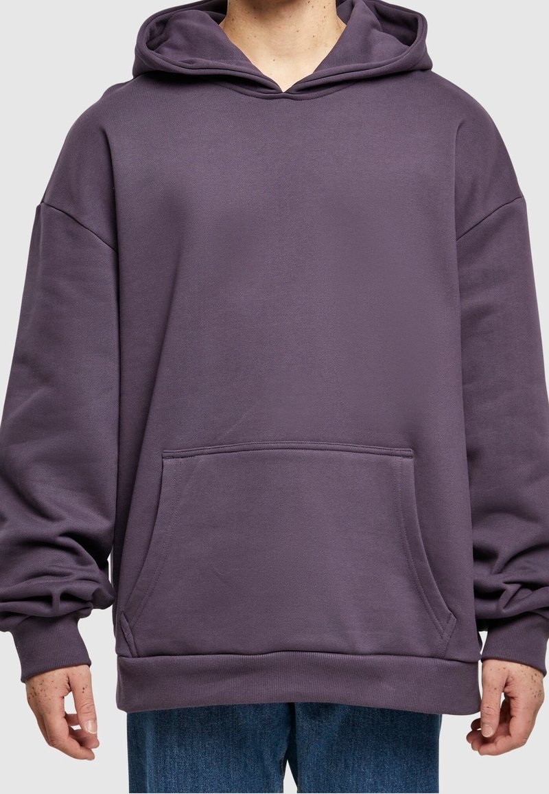 Un sweat à capuche violet avec une grande poche avant, coupe ample et capuche avec cordon de serrage. Fabriqué en tissu doux avec des poignets et un ourlet côtelés.