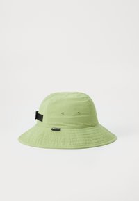 Chapeau seau vert clair avec un large bord, fabriqué en tissu texturé, doté d'œillets de ventilation et d'une sangle noire réglable.