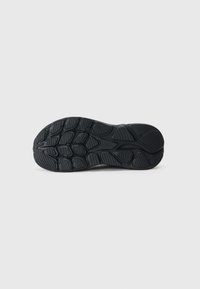 Semelle de sneaker en caoutchouc noir avec des motifs de texture et des détails de logo, mettant en avant des grips surélevés et des formes géométriques pour une meilleure traction.