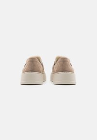 Suedesneakers i lys brun, med en myk foring, en hvit gummisåle og kontrasterende mørke detaljer ved hælen. Glatt tekstur.