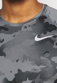 Grå camouflagemönstrad träningsskjorta med en slät struktur. Har en rund halsringning och en vit Nike-logotyp på bröstet.
