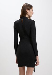Vestito mini nero a maniche lunghe con una silhouette aderente, texture shimmer, dettaglio con apertura a chiave sul retro e spacco laterale.