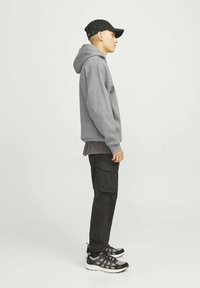 Sweat à capuche gris, casquette noire, pantalon cargo noir avec poches, et baskets gris/noir. Caractéristiques : coupe décontractée et design superposé.
