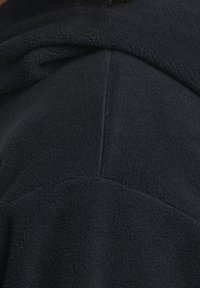 Tmavě modrá fleecová mikina s kapucí, která nabízí měkkou strukturu, volný střih a zaoblenou kapuci. Na zadní straně jsou viditelné švy.