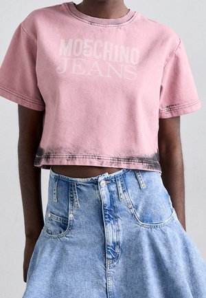 Persona con una camiseta rosa corta con el texto "MOSCHINO JEANS" y una falda vaquera de tiro alto en azul claro.