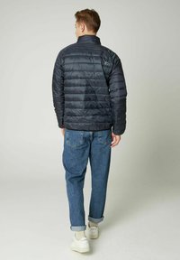 Tamsiai pilkas pūkinis švarkas su aukšta apykakle ir horizontaliais siuvinėjimo detalėmis, derinamas su suknežintomis šviesiai mėlynomis džinsomis ir baltomis sportbačiais.