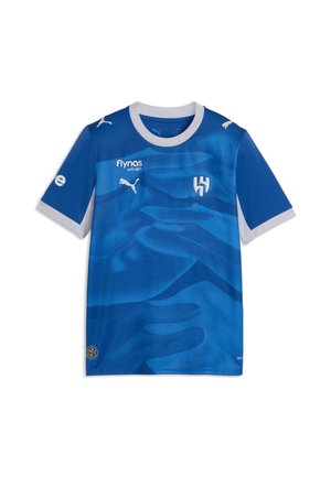 Blå fodboldtrøje med hvid krave og manchetter, Puma-logoer, Flynas-sponsor og en stiliseret H-emblem på brystet.