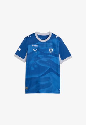 Blaues Fußballtrikot mit weißem Kragen und Bündchen, Puma-Logos, Flynas-Sponsor und einem stilisierten H-Emblem auf der Brust.