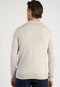 Jasnobeżowy, długi sweter z długim rękawem, z ryżowym kołnierzem i mankietami; gładka tekstura i dopasowany krój, widoczny z tyłu.