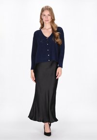 Cardigan tricotat bleu marin cu guler în V și nasturi, asortat cu o fustă maxi din satin negru, creând o siluetă elegantă.