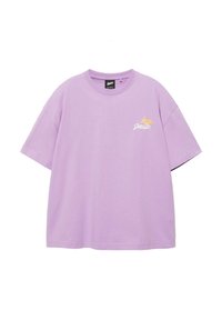 T-shirt lilas à manches courtes avec col rond, petit motif blanc et jaune sur la poitrine gauche et étiquette de marque noire à l'intérieur du col.