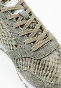 Grüner Sportschuh mit mesh-Obermaterial, Wildleder-Akzenten, Schnürdesign und strukturierter Sohle mit sichtbaren Nahtdetails.