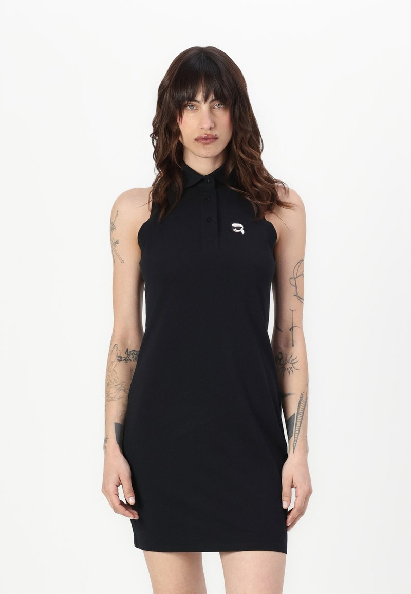 Vestido polo negro con cuello, diseño sin mangas y un pequeño logo en el pecho. Textura suave y silueta ajustada.