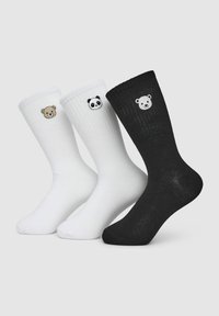 Tre paia di calzini a coste: due bianchi con design di orso e panda, e uno nero con un design di orso. Realizzati in un morbido materiale a coste.