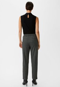 Black sleeveless top with a keyhole back; gray, checkered trousers with a relaxed fit and elastic waistband; worn with black high-heeled shoes.