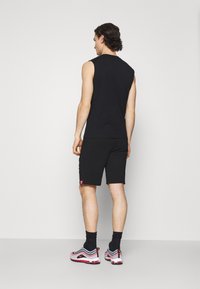 Svart ärmlös skjorta i kombination med svarta shorts. Accentuerad med en liten rosa logotyp, med ett mjukt tyg och atletisk passform. Sneakers i grått, röd och svart.