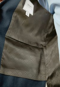 Marineblaues Sakko mit einem gemusterten schwarzen Innenfutter. Verfügt über ein "NEXT Tailoring"-Etikett und hat eine glatte Textur mit geometrischen Designs.