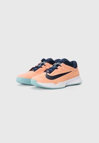 Persikų ir jūrų laivyno spalvos sportiniai bateliai su tekstūruotu tinkleliu, kontrastinga swoosh logotipu ir šviesiai mėlynu padu, kuriame yra sukibimo raštas.