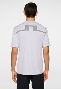 Ljust grå kortärmad t-shirt med ett mönstrat ryggdesign och en solid horisontell detalj. Tillverkad av mjukt och andningsbart tyg.