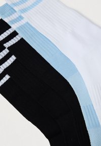 Kolm paari ribaga sokke: valged helesiniste triipudega, täielikult helesinised ja mustad valgete triipudega, paigutatud kattega.