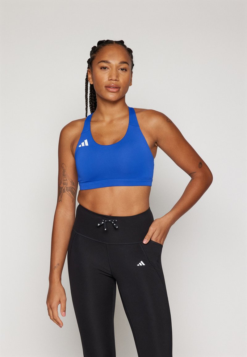 Blå sports-bh med rund halslinning, brede stropper og hvit logodetalj. Kombinert med svarte høytaljede tights med snor.
