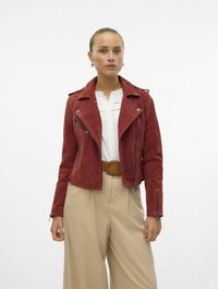 Rode suède motorjack met ritszakken, een reverskraag en een korte fit, gecombineerd met beige wijde broekspijpen en een bruine riem.