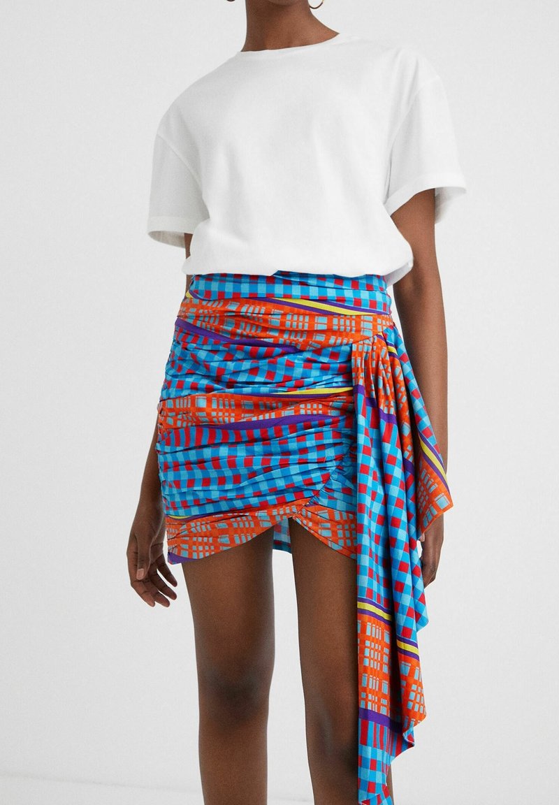 Valkoinen lyhythihainen t-paita yhdistettynä siniseen, punaiseen ja oranssiin kuviolyysiin, jossa on teksturoitu taitos ja epäsymmetrinen helma.