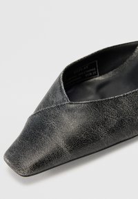 Chaussure en cuir noir avec un bout pointu, présentant une finition texturée et une silhouette basse. L'étiquette intérieure indique la taille EUR 37.