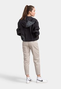 Zwarte lichtgewicht jas met grijze accenten, capuchon en een ontspannen pasvorm. Beigekleurige broek en witte high-top sneakers maken de outfit compleet.