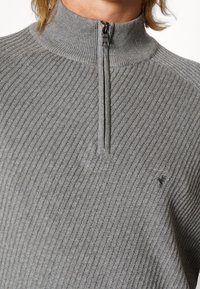 Grau gerippter Strickpullover mit hohem Kragen und Viertelreißverschluss. Mit kleinem Emblem auf der Brust. WeicheTextur, elegantes Design.