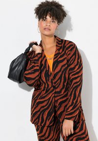 Blazer a strisce zebrate arancioni e nere con chiusura a un solo bottone, abbinato a un top arancione brillante e con in mano una borsa nera.