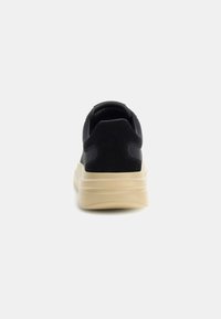 Sneaker nera con una toma liscia, punta arrotondata e suola chiara con dettagli testurizzati sul tallone e sui lati.