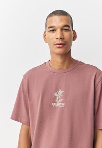 Relaxed-fit, short-sleeve t-shirt in dusty rose, featuring a white botanical graphic and text print on the front. Soft fabric texture.