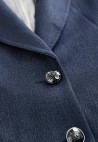 Marineblauer Denim-Blazer mit Reverskragen, einem glänzenden schwarzen Knopf mit geprägtem Design und subtiler Textur im Stoff.