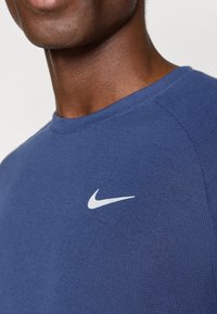 Ναυτικό μπλε αθλητικό μπλουζάκι Nike με ριγέ υφή, που διαθέτει μια λευκή λογότυπα στην αριστερή πλευρά του στήθους και στρογγυλή λαιμόκοψη.