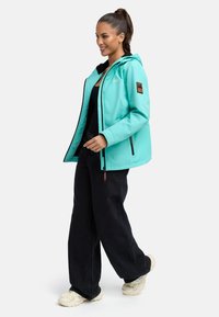 Turquoise waterproof jacket with a hood, black lining, tan accents on the sleeve, paired with black wide-leg pants and beige sneakers.