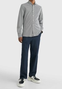 Camisa de botones a rayas en azul marino y blanco, combinada con pantalones azul marino y zapatillas blancas y negras, con un corte slim y textura suave.