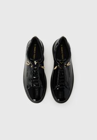 Zapatillas de charol negras con herrajes decorativos en tono dorado, cordones elásticos y un diseño elegante. Tamaño 37 marcado en el interior.
