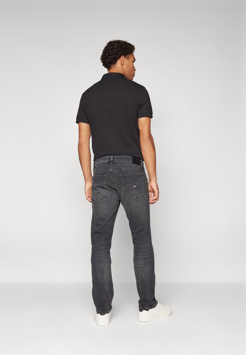 Polo negro combinado con jeans gris oscuro. Los jeans tienen un diseño sencillo con bolsillos traseros. Zapatillas blancas completan el atuendo.