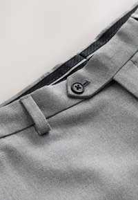 Close-up of gray fabric pants with a black button and belt loop on the waistband, showing detailed stitching and inner lining.