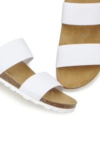 Witte sandalen met twee brede elastische banden, een kurken voetbed en een gewelfde witte zool. Het ontwerp is minimalistisch en praktisch.