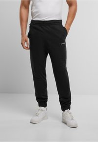 Zwarte sweatpants met een elastische tailleband, zijzakken en geribbelde manchetten. Heeft een klein wit logo op de linker dij.