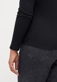 Top negro de manga larga con canalé, con un dobladillo redondeado, combinado con unos vaqueros de mezclilla gris oscuro, que muestran una textura de tela y detalles en el bolsillo trasero.