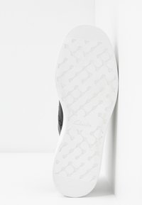 Semelle de chaussure en caoutchouc blanc avec des motifs de rainures circulaires et connectives et un petit logo "Clarks" embossé près de la zone de la voûte plantaire.