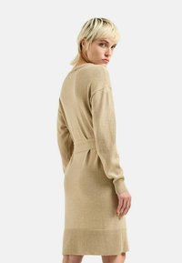 Abito lavorato a maglia in beige chiaro con maniche lunghe e vita con cintura. Presenta una stoffa testurizzata e un orlo a coste all'altezza del ginocchio.