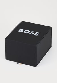 Black box with a smooth matte finish, featuring the white word "BOSS" on the top. Includes a small multi-colored ribbon on the side.